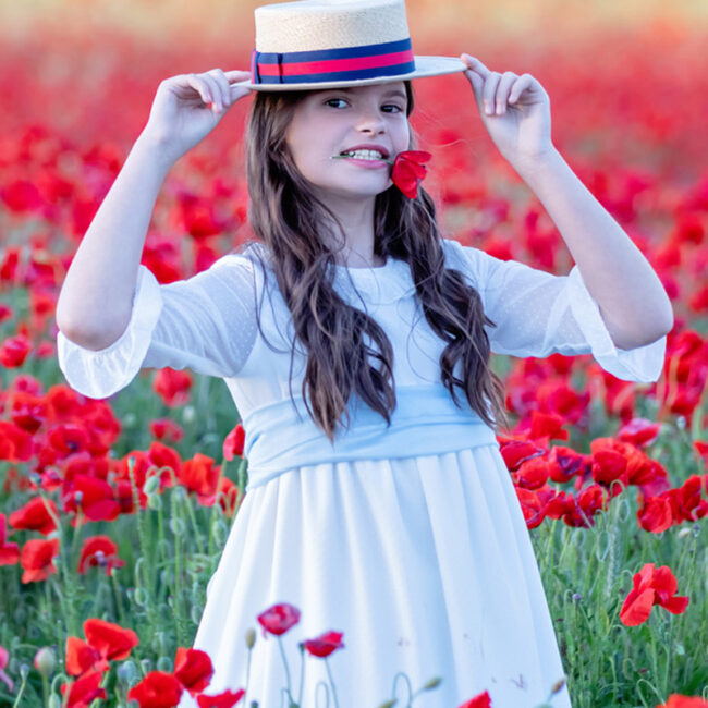 Retrato de comunión de una niña con vestido blanco y sombrero entre amapolas